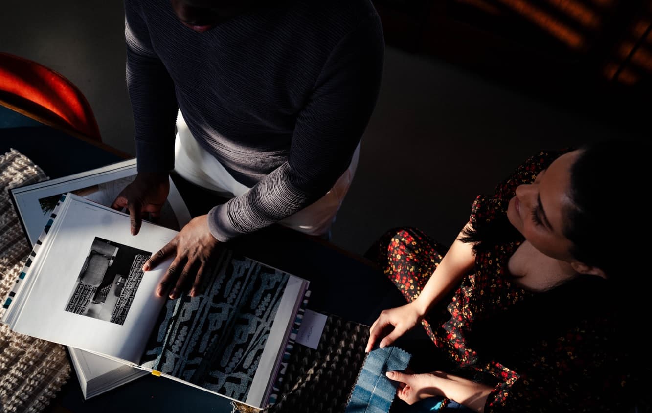 Overhead shot of two team members reviewing designs and fabrics in a dimly lit room
